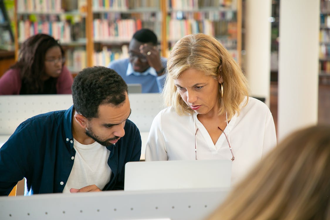 Free Serious ethnic bearded male student preparing study task and explaining project details to teacher in university library Stock Photo